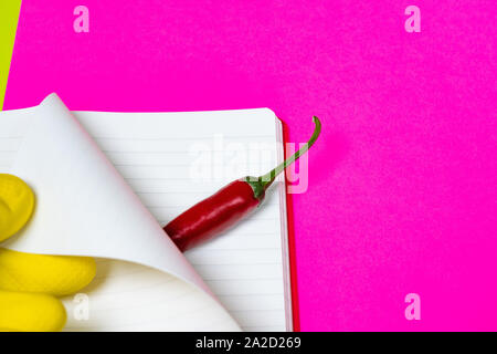 Hands in rubber gloves carefully turn over the page of an empty magazine and open burning red pepper. Bright pink and yellow background. Stock Photo