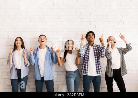 Teen friends pointing up on free space over white wall Stock Photo