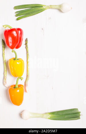 Mixed peppers and spring onions in a border frame on a light wooden kitchen surface Stock Photo