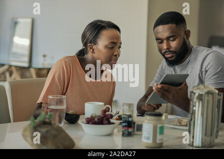 Smiling young African American couple using a tablet over breakfast Stock Photo