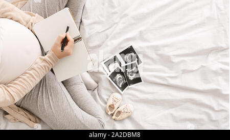 Pregnant woman noting noting down thoughts in bed Stock Photo