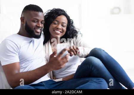 Happy African American couple using smartphone, surfing internet at home Stock Photo