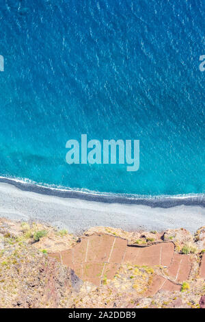 Aerial landscape by the blue Atlantic ocean. Stone beach and adjacent fields on the southern coast of Madeira Island, Portugal. Aerial view, amazing nature. Summer vibes on a vertical photo. Stock Photo
