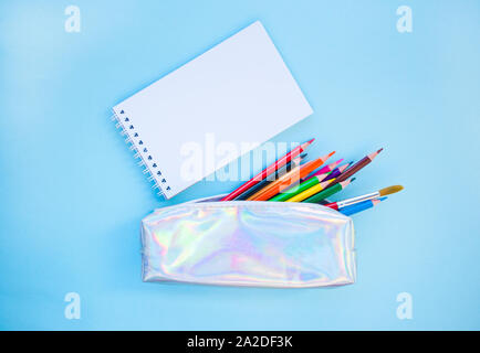 Colorful pencils, watercolors, holographic pencil box on blue background with copyspace. Flat lay style. Back to school concept. Stock Photo