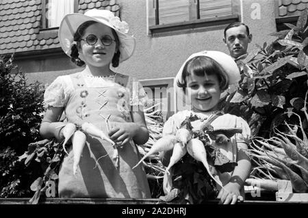 Zwei kleine Mädchen auf dem firmeneigenen Festwagen des Rettich Versands Hanacker beim Festumzug zum Rettichfest in Schifferstadt, Deutschland 1930er Jahre. Parade float of the radish dispatch company Hanacker with a staff member and two little girls at the pageant of the annual radish fair at Schifferstadt, Germany 1930s. Stock Photo