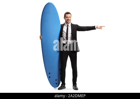 Full length portrait of a man in a suit holding a surfing board and pointing to the side isolated on white background Stock Photo