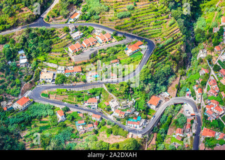 Aerial view of a village Curral das Freiras, Madeira Island, Portugal. Rural houses, green terraced fields, and scenic serpentine road photographed from above. Aerial landscape. Travel destination. Stock Photo