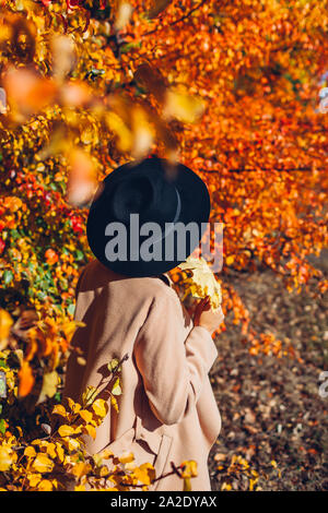 Autumn vibes. Young woman walking in autumn forest among falling leaves. Stylish girl wearing hat and holding leaves Stock Photo