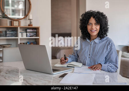 Smiling young female entrepreneur working from home on a laptop Stock Photo