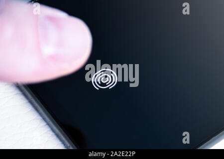 Unlocking the phone with the finger on a digital fingerprint scanner built in under the screen close up Stock Photo