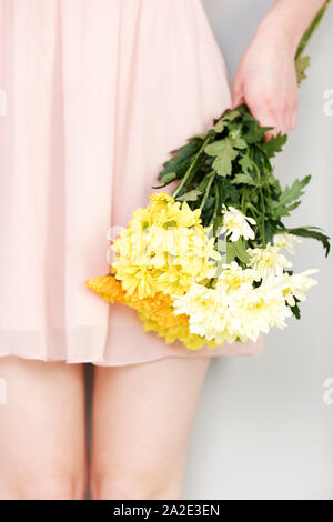 A cropped view of a woman holding fresh flowers in a pink dress. Stock Photo