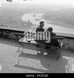 Ein Paar sitzt auf einer Bank und sieht auf die Stadt Koblenz und die Moselmündung beim Deutschen Eck, Deutschland 1930er JAhre. A couple at a bench watching the city of Koblenz and the confluence of Rhine and Moselle at the Deutsches Eck, Germany 1930s.