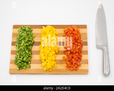 Red, green and yellow sweet bell peppers chopped on a wooden cutting board and a cutting knife Stock Photo