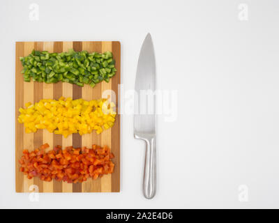 Red, green and yellow sweet bell peppers chopped on a wooden cutting board and a cutting knife Stock Photo