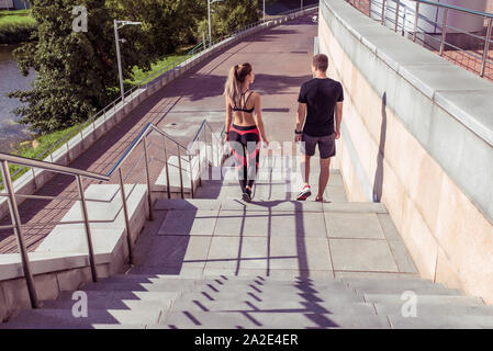 Young couple man woman go up stairs, view from back, in summer, autumn and spring in city, free space for motivation text, sportswear, active fitness Stock Photo