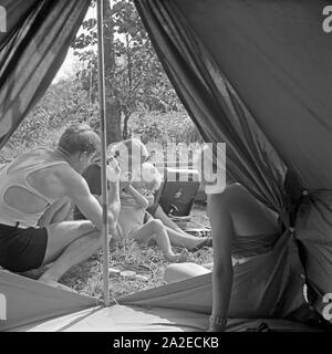 Campingausflug ans Ufer eines Sees, wo die Familie um ein Electrola Koffer 106 Grammophon sitzt, Deutschland 1930er Jahre. Camping trip to the shore of a lake, where the family is listening to music, played by an Electrola Koffer 106 suitcase gramophone, Germany 1930s. Stock Photo
