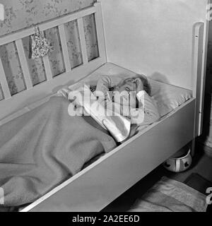 Ein kleiner Junge stellt sich schlafend in seinem Kinderbett, Deutschland 1930er Jahre. A little boy pretending to sleep, Germany 1930s. Stock Photo