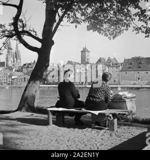 Zwei Frauen sitzen mit einem Kinderwagen am Ufer der Donau in Regensburg, Deutschland 1930er Jahre. Two women with a pram sitting on the shore of river Danube at Regensburg, Germany 1930s. Stock Photo