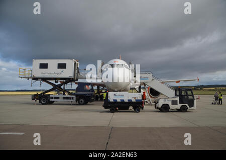An EasyJet Airbus A319-111 parked on the concrete apron surrounded by various service vehicles at Inverness Dalcross Airport, Scottish Highlands, UK. Stock Photo