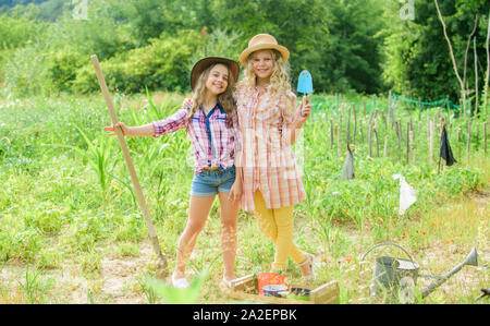 Growing vegetables. Hope for nice harvest. Girls planting plants. Rustic children working in garden. Planting and watering. Agriculture concept. Sisters together helping at farm. Planting vegetables. Stock Photo