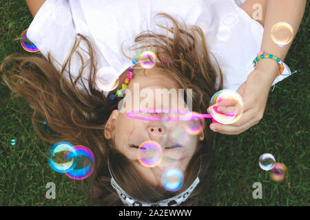 Top view of a beautiful little girl laying on the grass, blowing soap bubbles