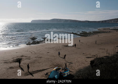 View of Compton Beach at low tide in summer with late afternoon sun and beachgoers playing ball games Stock Photo