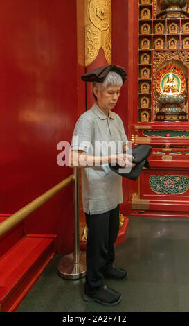 Singapore - March 22, 2019: Buddha Tooth Relic Temple in Chinatown. Female attendant distributes dark brown folded robes while carrying them on her he Stock Photo