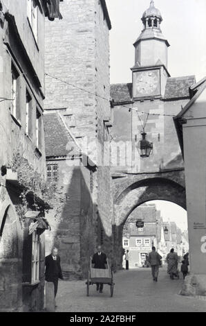 Ein geschäftiges Treiben herrscht auf der Straße vor einem der zahlreichen Türme mit Torbogen in Rothenburg ob der Tauber, Deutschland 1930er Jahre. A hustle and bustle on a street with one of the many towers and archways in Rothenburg ob der Tauber, Germany 1930s. Stock Photo