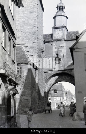 Ein geschäftiges Treiben herrscht auf der Straße vor einem der zahlreichen Türme mit Torbogen in Rothenburg ob der Tauber, Deutschland 1930er Jahre. A hustle and bustle on a street with one of the many towers and archways in Rothenburg ob der Tauber, Germany 1930s. Stock Photo