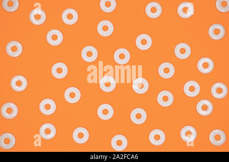 Flat round white plastic beads in irregular pattern on orange cardboard background Stock Photo
