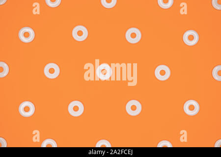 Flat round white plastic beads in regular pattern on orange cardboard background Stock Photo