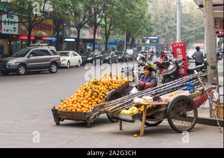 Hunan, China, 14 Nov 2011: Asian female senior selling fruits along street in busy city downtown. Stock Photo