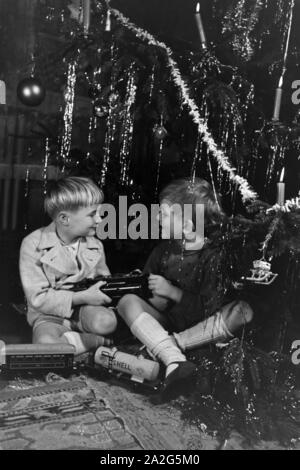 Zwei Jungen streiten am Weihnachtsabend unter dem Tannenbaum um die neue Modelleisenbahn, Deutschland 1938. Two boys quarrelling about the new model train under the christmas tree, Germany 1930s Stock Photo