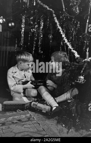 Zwei Jungen streiten am Weihnachtsabend unter dem Tannenbaum um die neue Modelleisenbahn, Deutschland 1938. Two boys quarrelling about the new model train under the christmas tree, Germany 1930s Stock Photo