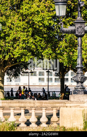 People sitting on Garonne river bank in Bordeaux, France, with a river cruise ship going through Stock Photo
