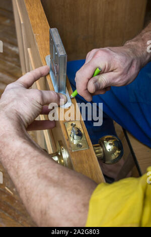 Carpenter doing on old wooden door the markup for the mortise lock using a pencil. Stock Photo