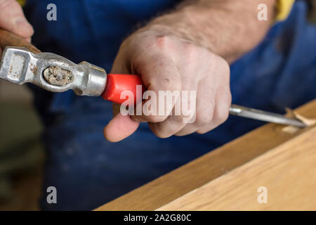 Carpenter makes a hole in old wooden door for the mortise lock with a hammer and chisel. Close-up. Stock Photo