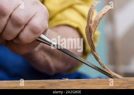 Carpenter makes a hole in old wooden door for the mortise lock with a hammer and chisel. Close-up. Stock Photo