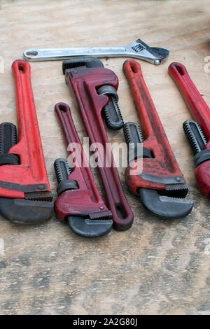 A row of pipe wrenches and an adjustable wrench are laid out on plywood at a garage sale Stock Photo