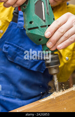 Carpenter makes a hole in old wooden door the mortise lock for by using power drill. Close-up. Stock Photo