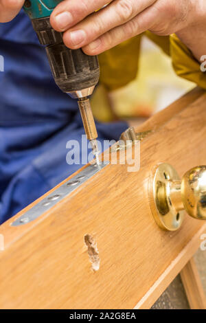 Carpenter attach using the screwdriver mortise lock in an old wooden door. Stock Photo