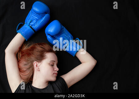 A girl in boxing gloves lies on the floor with her eyes closed in a knockout Stock Photo