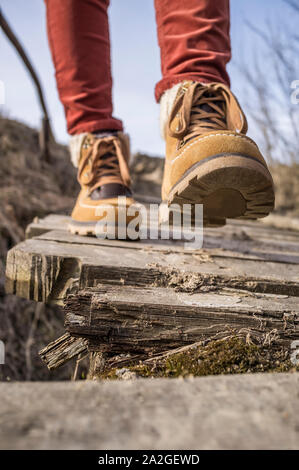 Girl walks along the old rotten wooden bridge in stylish boots, on a spring sunny afternoon. Stock Photo