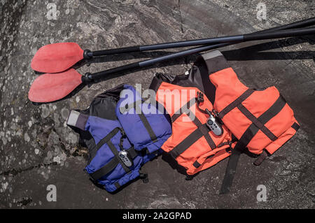 Two life jackets and a radio are on the rocky coast, near lie oars. Stock Photo