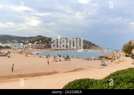 TOSSA DE MAR, SPAIN - AUGUST 7, 2019: Sunbathing people on a central city beach in summer by the sea. Sunlight, green in the foreground Stock Photo