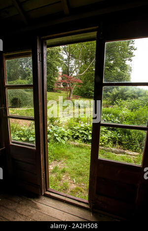 View of a lush garden through the doors and windows of a wooden summer house Stock Photo