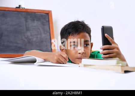 Boy playing with smartphone while doing homework Stock Photo