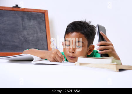 Boy playing with smartphone while doing homework Stock Photo