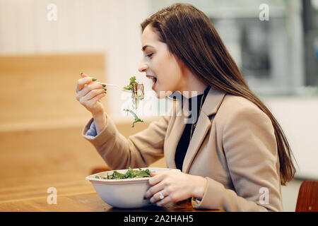 Girl eats vegetable salad. Lady sitting in a cafe. Brunette in a brown coat Stock Photo