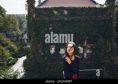 beautiful brunette posing on a staircase with breathtaking background of a building covered in ivy Stock Photo